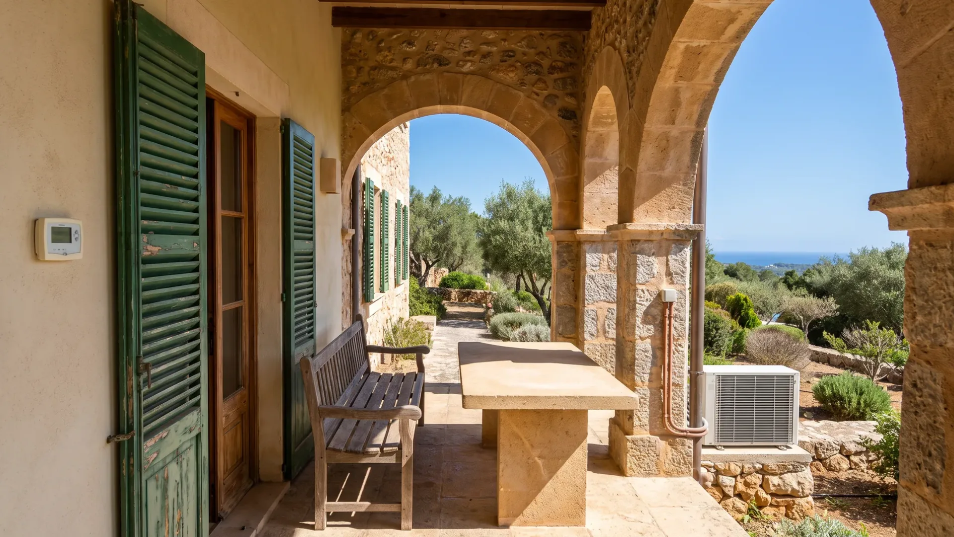 A terrace under a stone arch with a bench and table, a condenser beside it and the sea beyond