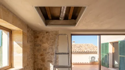 An opened ceiling void with flexible duct above a step ladder, a condenser on the terrace beyond