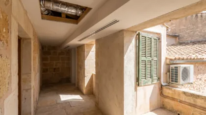 A slot diffuser and open ceiling void in a stone passage, a wall condenser beyond the window