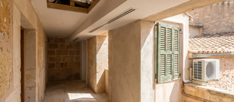 Un difusor lineal y un falso techo abierto en un pasillo de piedra, una unidad exterior de pared tras la ventana