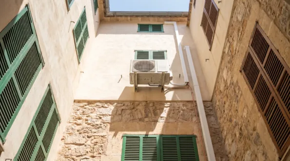 A condenser bracketed high in a narrow rendered light well, shuttered windows on every side