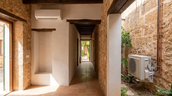 A wall unit at the head of a long tiled passage, a condenser on the wall in the courtyard outside