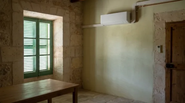 A wall unit on a pale green wall in a plain room with a timber table and a shuttered window
