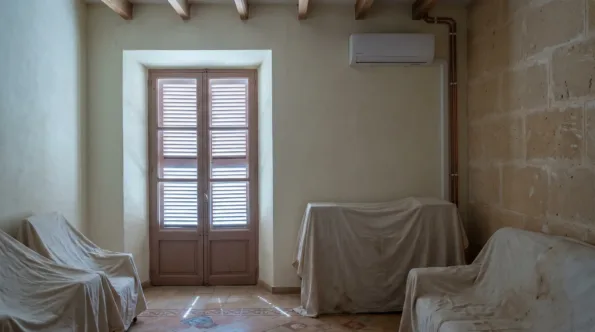 A wall unit above dust sheeted furniture in a shuttered room, copper pipe run to the corner