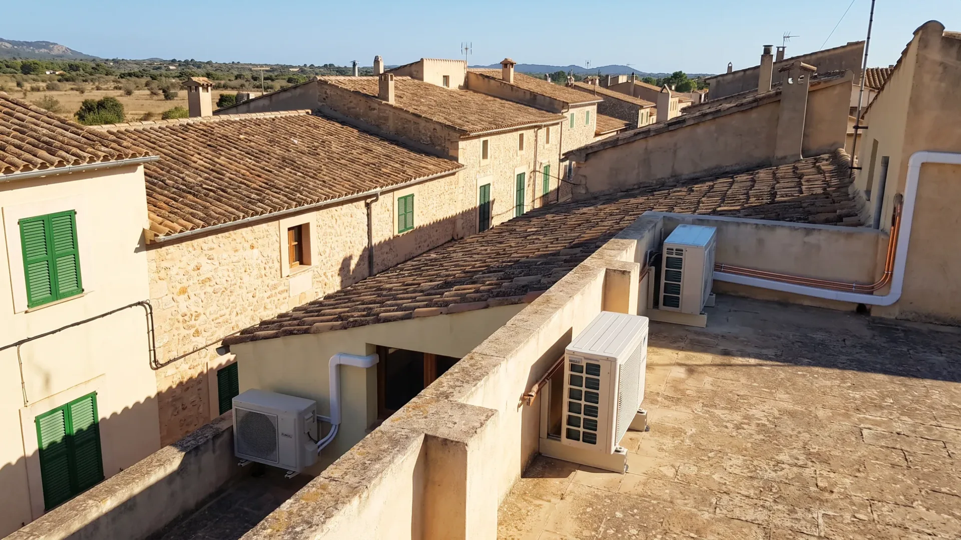 Condensers on a flat roof terrace among clay tiled roofs, pipe runs crossing the parapet