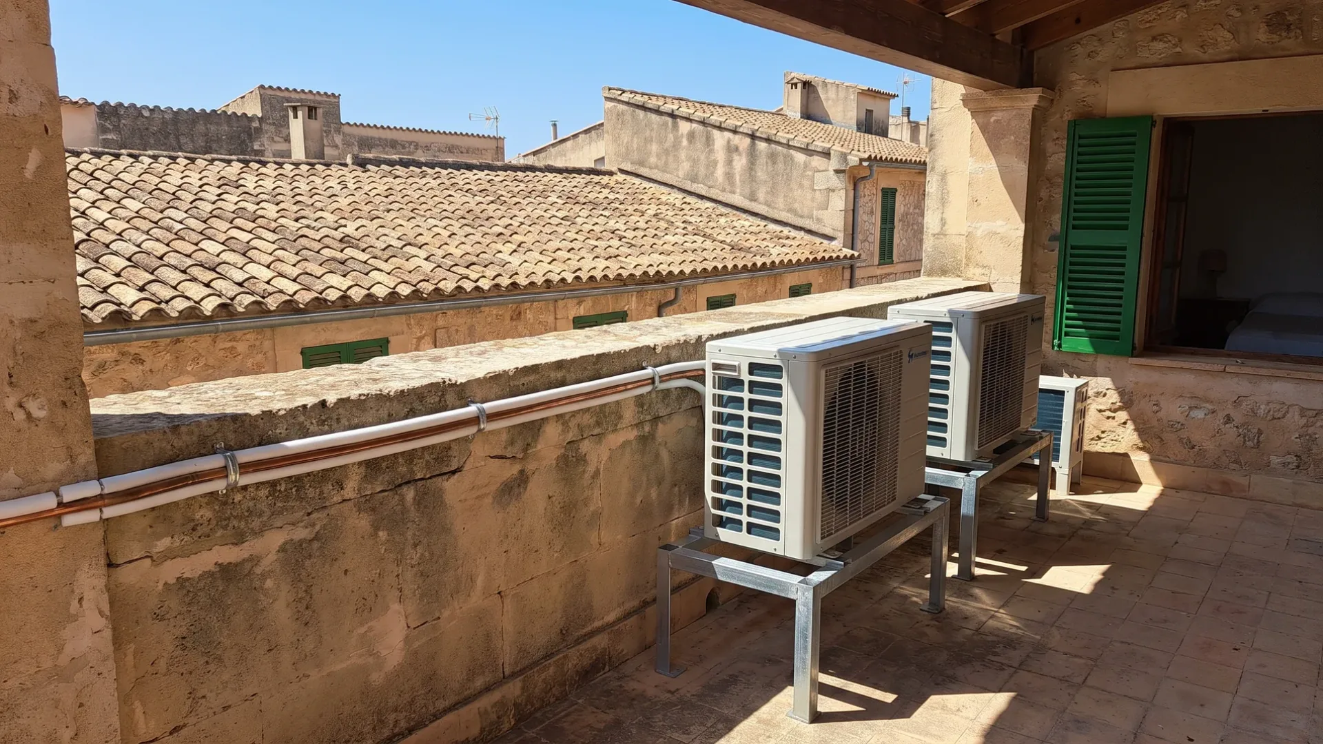 Two condensers on galvanised stands on a roof terrace above a roofscape of clay tiles