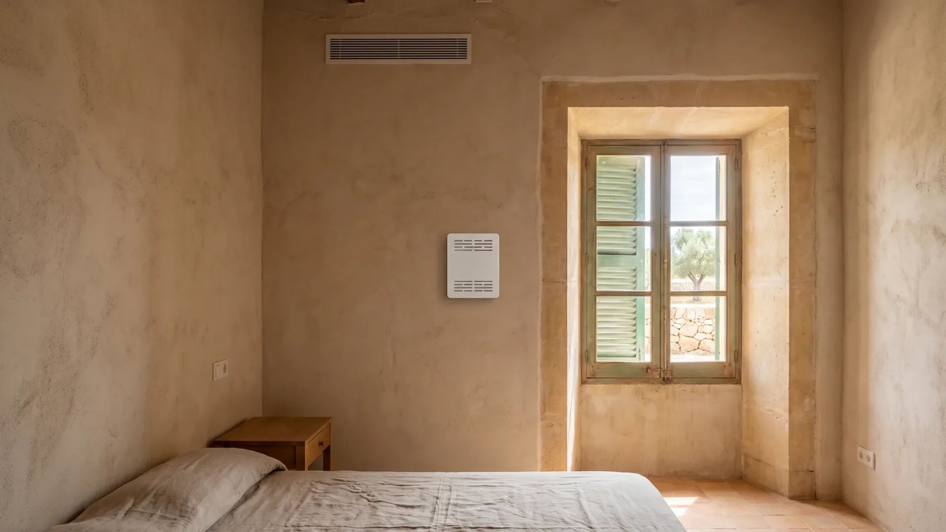 A small white wall control below a ceiling grille in a lime-plastered bedroom, shutters half open beside it