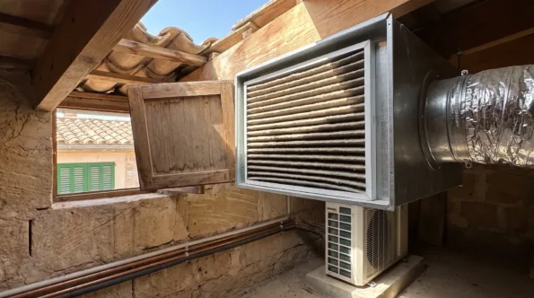 A duct-mounted filter box in a roof space, its pleated filter dark with dust and flexible duct on the outlet