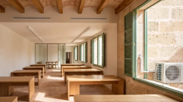 Two linear diffusers in a vaulted beamed ceiling above plain timber desks in a long shuttered workroom